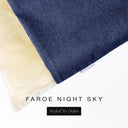 A close up detail of the corner of a Charley Chau Burrow Bag Dog Bed with dark navy blue outer cover in woven wool texture upholstery fabric Faroe and plush cream faux-fur lining with a woven brand label showing the Charley Chau logo on a white backdrop.