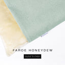A close up detail of the corner of a Charley Chau Burrow Bag Dog Bed with pale sage green outer cover in woven wool texture upholstery fabric Faroe and plush cream faux-fur lining with a woven brand label showing the Charley Chau logo on a white backdrop.