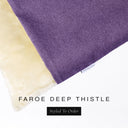 A close up detail of the corner of a Charley Chau Burrow Bag Dog Bed with dusty purple outer cover in woven wool texture upholstery fabric Faroe and plush cream faux-fur lining with a woven brand label showing the Charley Chau logo on a white backdrop.
