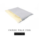 A luxurious Dog Burrow Bag, a sleeping bag style dog bed or snuggle sack style dog bed, with an outer cover in pale grey woven wool texture upholstery fabric Faroe with a plush, cream faux-fur lining, and a badge with the colour name Pale Fog on a white background.