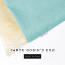 A close up detail of the corner of a Charley Chau Burrow Bag Dog Bed with pale aqua outer cover in woven wool texture upholstery fabric Faroe and plush cream faux-fur lining with a woven brand label showing the Charley Chau logo on a white backdrop.