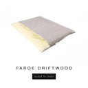 A luxurious Dog Burrow Bag, a sleeping bag style dog bed or snuggle sack style dog bed, with an outer cover in pale taupe grey woven wool texture upholstery fabric Faroe with a plush, cream faux-fur lining, and a badge with the colour name Driftwood on a white background.