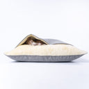 A dog sleeping very cosy in a burrow bed style luxury dog snuggle bed in a grey outer fabric with a cream faux-fur lining ona white backdrop. 