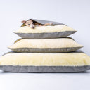 A stack of three luxury dog snuggle beds, cave bed style dog beds, with a dog lying isde the top snuggle bed on a white backdrop.
