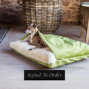 Dog lying inside a cave bed style luxury dog bed, the Charley Chau Snuggle Bed, with a lime green velvet outer cover and push cream lining in a home setting with a rattan basket in the background.