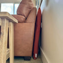 An orange luxury travel pad mattress staored standing up on its side behind a brown leather sofa in a home setting.