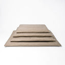 Four luxury dog travel mattress pads in a beige woven upholstery fabric in different sizes stacked on a white backdrop.