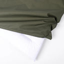 A tough, water-resistant dog crate mattress in olive green being removed from the white crate pad insert inside on a white backdrop.