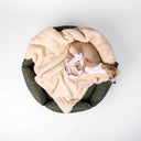 Top-down view of an olive/khaki green, water-resistant donut style dog bed with a beige sherpa fleece blanket and a dog sleeping cosily inside, on a white background.