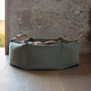 A dog lying in a luxury donut dog bed with hig-sides and resting its chin on the side of the bed.