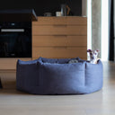 A dog peeking its head above the high sides of a luxury dont dog bed in dark grey in a contemporay home kitchen setting with woode floor.