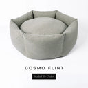 A luxury donut dog bed in pale flint grey-green Cosmo fabric, suitable for all breeds of dogs, with cosy high-wall sides and a deep-filled luxury mattress inside, on a white background with the text 'COSMO FLINT' and 'Styled To Order' below.