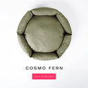 A top-down view of a muted khaki-green luxury donut dog bed with high-wall padded sides and a round mattress inside, on a white background with the text 'COSMO FERN' and a pink 'Core Collection' label below.