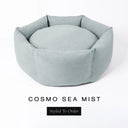 A luxury donut dog bed in pale sea-mist grey-green Cosmo fabric, suitable for all breeds of dogs, with cosy high-wall sides and a deep-filled luxury mattress inside, on a white background with the text 'COSMO SEA MIST' and 'Styled To Order' below.