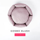A top-down view of a pale dusty pink luxury donut dog bed with high-wall padded sides and a round mattress inside, on a white background with the text 'COSMO BLUSH' and a pink 'Core Collection' label below.