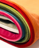 Stack of brightly coloured velvet dog bed covers on a white background