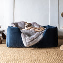 A picture of an Italian Greyhound looking super comfy on top of a pale purple Lilac Rabbit Faux Fur Dog Blanket that has been placed inside of a dark blue deep sided bed in navy velvet, both are machine washable.