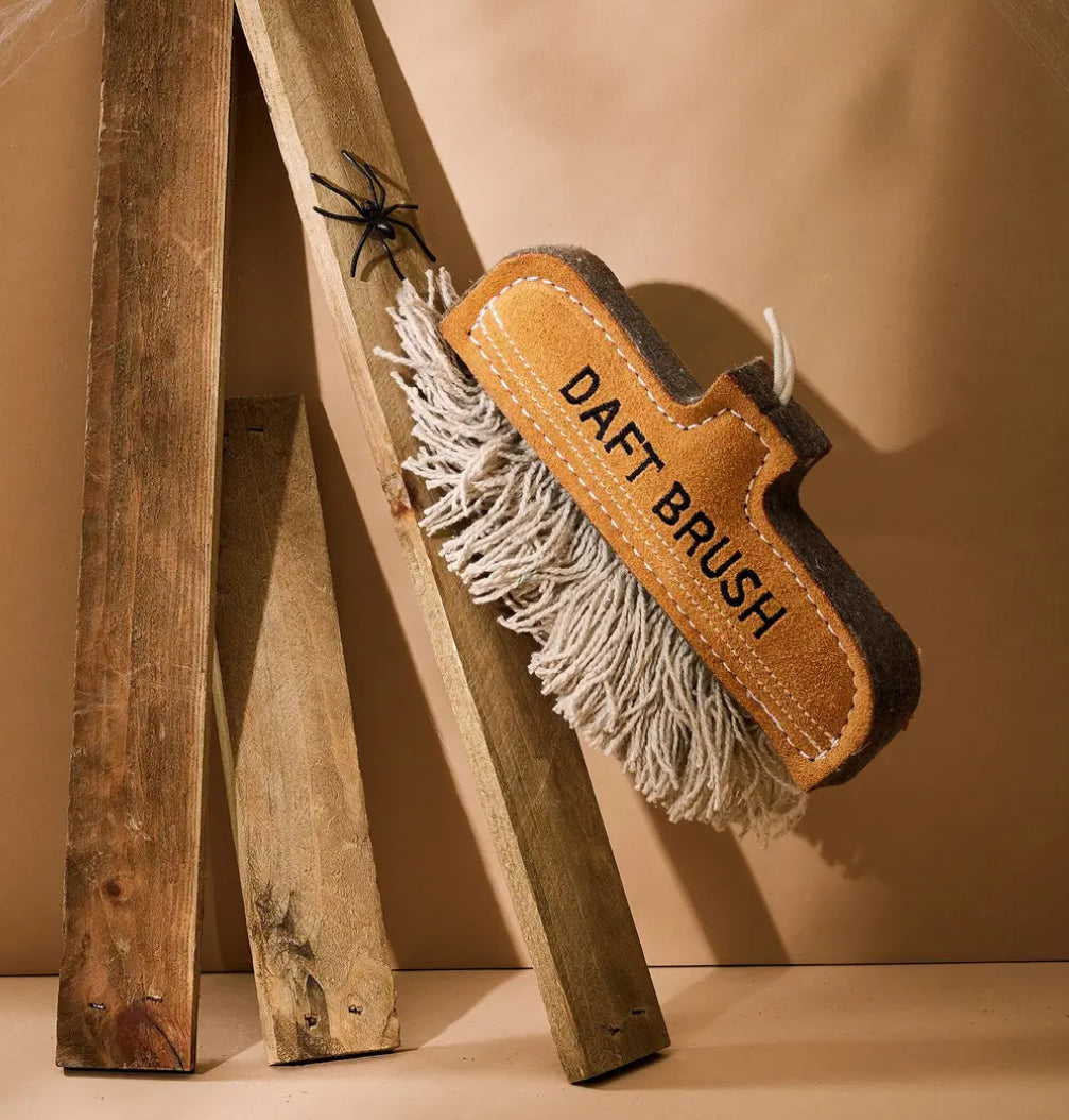 Dog toy brush with 'Daft Brush' branding on a wooden stand against a beige background.