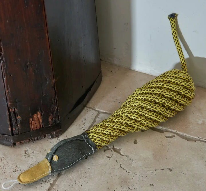 Yellow duck, dog toy on a  concrete floor next to a wooden cabinet.