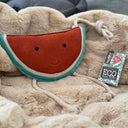Watermelon shaped dog toy with a smiling face and rope legs and handle, sitting on a luxury fawn faux-fur dog blanket