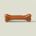 A brown, bone-shaped, natural dog chew treat made from Madeira Cheese and Peanut Butter on a pale sage green background.