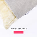 A close up detail of the corner of a Charley Chau Dog Snuggle Bed with pale beige upholstery-quality woven-wool texture fabric Faroe, and plush cream faux-fur lining with a woven brand label showing the Charley Chau logo on a white backdrop.