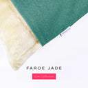 A close up detail of the corner of a Charley Chau Dog Snuggle Bed with jade green outer cover in upholstery-quality woven-wool texture fabric Faroe, and plush cream faux-fur lining with a woven brand label showing the Charley Chau logo on a white backdrop.