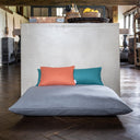 Two Mini Bolster Pad cushions in jade green and orange on a grey luxury deep-filled dog bed mattress in a home setting with a dark wooden floor.