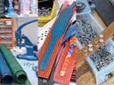 A collage of images of Petiquette Leather Dog Collars being handcrafted with leather and crafting tools and materials, including a blue leather punch, rolls of green and blue leather, colorful leather collars cut waiting to be stitched,  and a brown leather dog collar with Swaorvski crystals embellishments.