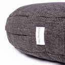 Close up shot of a round luxury dog bed mattress made with a dark brown/black woven upholstery fabric with a Charley Chau designer brand label on a white backdrop. 