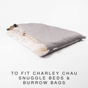 A small dog lying inside a luxury dog burrow bag, a snuggle sack style dog bed or sleeping bag style dog bed, with a pale grey Velour outer cover and plush, cream faux-fur lining on a white backdrop.