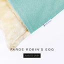 A close up detail of the corner of a Charley Chau Dog Snuggle Bed and dog Burrow Bag Dog Bed Cover with pale aqua outer cover in woven wool texture upholstery-quality Faroe and plush cream faux-fur lining with a woven brand label showing the Charley Chau logo on a white backdrop.