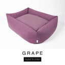 A dusky mauve-purple Bliss Bolster Dog Bed in 'GRAPE' Faroe fabric shown from an angle on a white background, highlighting the tall sides of this long lasting dog bed with sides; a stylish bolster dog bed and high-wall dog bed for dogs of all sizes.