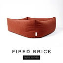 Close-up corner view of a warm terracotta orange-red Bliss Bolster Dog Bed in 'FIRED BRICK' Faroe fabric with a black 'Styled To Order' label, showing the tall walls of this long lasting dog bed with sides; a durable bolster dog bed and high-wall dog bed built to last.
