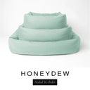 Three sizes of the Bliss Bolster Dog Bed in a pale sage green 'HONEYDEW' Faroe fabric nested together, showing this long lasting dog bed with sides in Small, Medium and Large; a hard-wearing bolster dog bed and high-wall dog bed for everyday comfort.