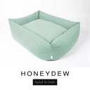 A pale sage green Bliss Bolster Dog Bed in 'HONEYDEW' Faroe fabric shown from an angle on a white background, highlighting the tall sides of this long lasting dog bed with sides; a stylish bolster dog bed and high-wall dog bed for dogs of all sizes.