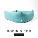 Close-up corner view of a soft powder blue Bliss Bolster Dog Bed in 'ROBIN'S EGG' Faroe fabric with a black 'Styled To Order' label, showing the tall walls of this long lasting dog bed with sides; a durable bolster dog bed and high-wall dog bed built to last.