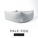 Close-up corner view of a soft pale grey Bliss Bolster Dog Bed in 'PALE FOG' Faroe fabric with a black 'Styled To Order' label, showing the tall walls of this long lasting dog bed with sides; a durable bolster dog bed and high-wall dog bed built to last.