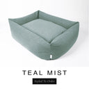 A muted sage teal Bliss Bolster Dog Bed in 'TEAL MIST' Faroe fabric shown from an angle on a white background, highlighting the tall sides of this long lasting dog bed with sides; a stylish bolster dog bed and high-wall dog bed for dogs of all sizes.