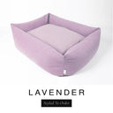 A soft dusky pink-lilac Bliss Bolster Dog Bed in 'LAVENDER' Faroe fabric shown from an angle on a white background, highlighting the tall sides of this long lasting dog bed with sides; a stylish bolster dog bed and high-wall dog bed for dogs of all sizes.