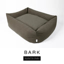 A deep olive brown Bliss Bolster Dog Bed in 'BARK' Faroe fabric shown from an angle on a white background, highlighting the tall sides of this long lasting dog bed with sides; a stylish bolster dog bed and high-wall dog bed for dogs of all sizes.