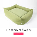 A soft sage green Bliss Bolster Dog Bed in 'LEMONGRASS' Faroe fabric shown from an angle on a white background, highlighting the tall sides of this long lasting dog bed with sides; a stylish bolster dog bed and high-wall dog bed for dogs of all sizes.