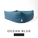 Close-up corner view of a deep petrol blue Bliss Bolster Dog Bed in 'OCEAN BLUE' Faroe fabric with a black 'Styled To Order' label, showing the tall walls of this long lasting dog bed with sides; a durable bolster dog bed and high-wall dog bed built to last.