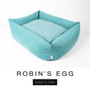 A soft powder blue Bliss Bolster Dog Bed in 'ROBIN'S EGG' Faroe fabric shown from an angle on a white background, highlighting the tall sides of this long lasting dog bed with sides; a stylish bolster dog bed and high-wall dog bed for dogs of all sizes.