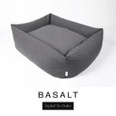 A dark charcoal grey Bliss Bolster Dog Bed in 'BASALT' Faroe fabric shown from an angle on a white background, highlighting the tall sides of this long lasting dog bed with sides; a stylish bolster dog bed and high-wall dog bed for dogs of all sizes.