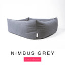Close-up corner view of a cool blue-grey Bliss Bolster Dog Bed in 'NIMBUS GREY' Faroe fabric with a pink 'Core Collection' label, showing the tall walls of this long lasting dog bed with sides; a durable bolster dog bed and high-wall dog bed built to last.