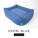 A rich denim blue Bliss Bolster Dog Bed in 'CAPRI BLUE' Faroe fabric shown from an angle on a white background, highlighting the tall sides of this long lasting dog bed with sides; a stylish bolster dog bed and high-wall dog bed for dogs of all sizes.