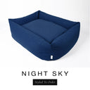 A deep navy blue Bliss Bolster Dog Bed in 'NIGHT SKY' Faroe fabric shown from an angle on a white background, highlighting the tall sides of this long lasting dog bed with sides; a stylish bolster dog bed and high-wall dog bed for dogs of all sizes.