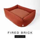 A warm terracotta orange-red Bliss Bolster Dog Bed in 'FIRED BRICK' Faroe fabric shown from an angle on a white background, highlighting the tall sides of this long lasting dog bed with sides; a stylish bolster dog bed and high-wall dog bed for dogs of all sizes.